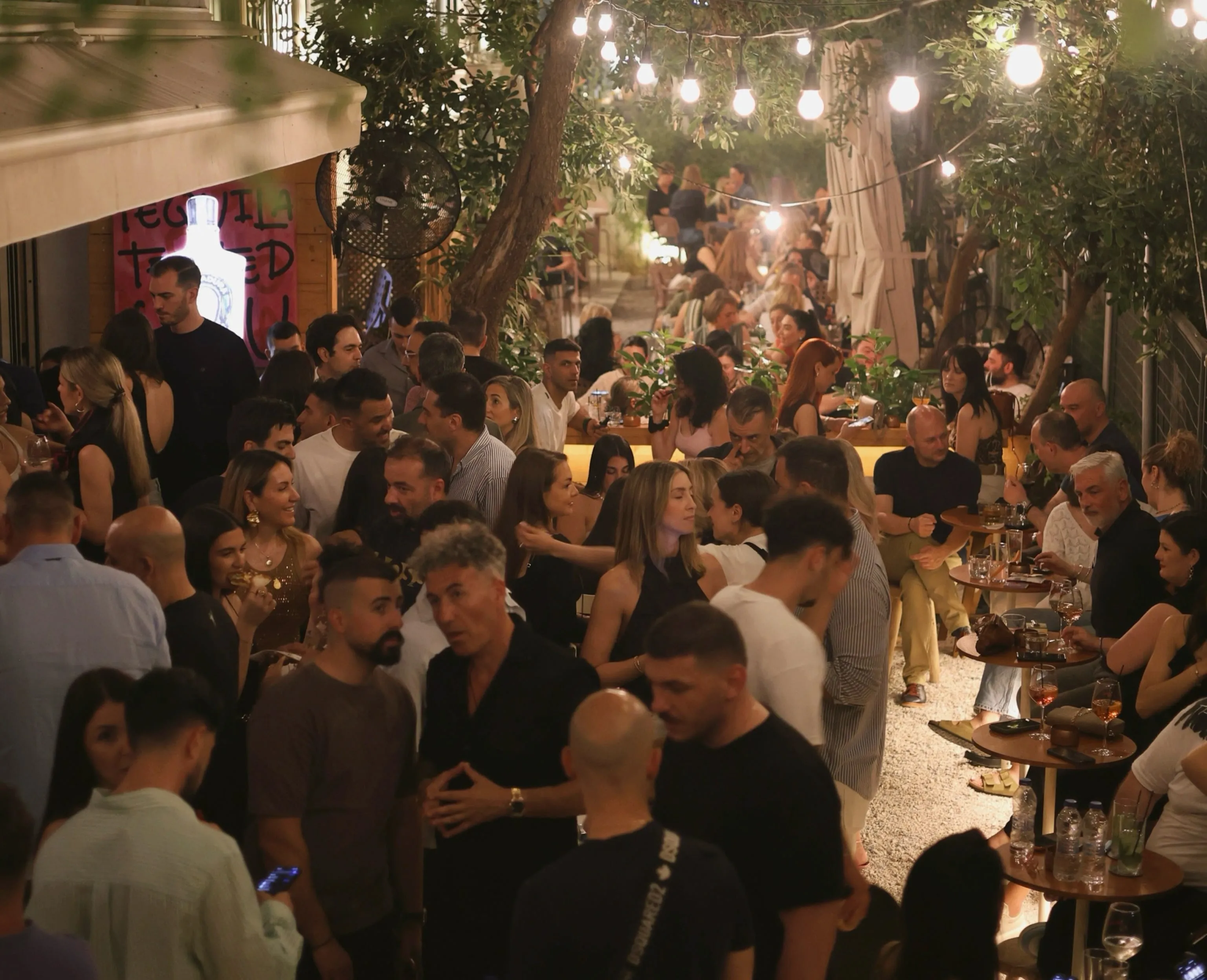 Η αυλή της Αφέσου το βράδυ, γεμάτη κόσμο κάτω από δέντρα και κρεμαστά φωτάκια