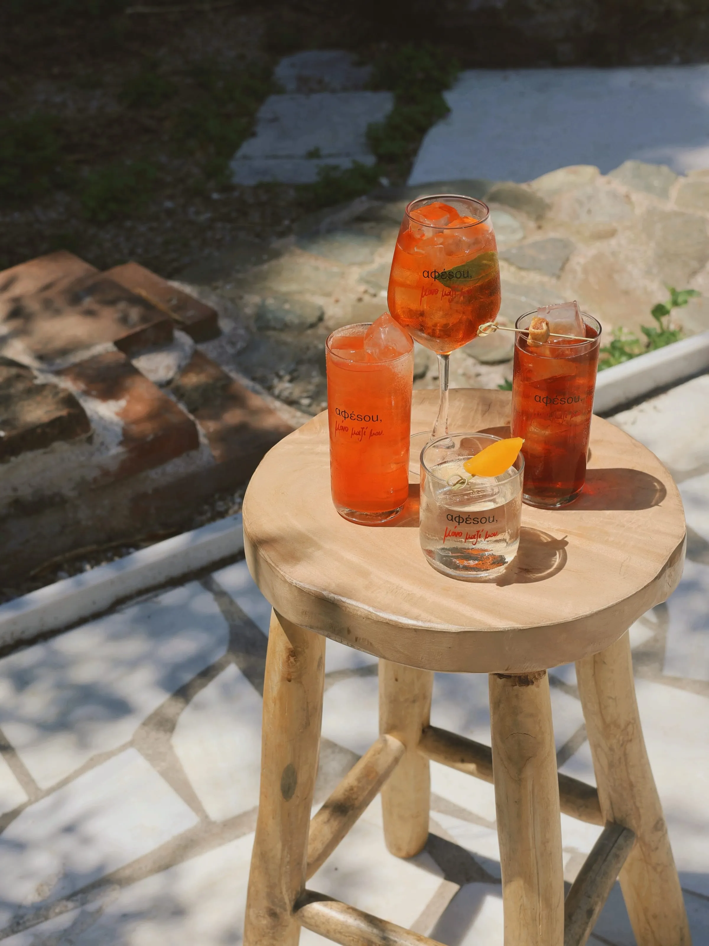 Τρία ποτήρια spritz με το λογότυπο «αφέσου, μόνο μαζί μου» σε ξύλινο σκαμπό στον ήλιο