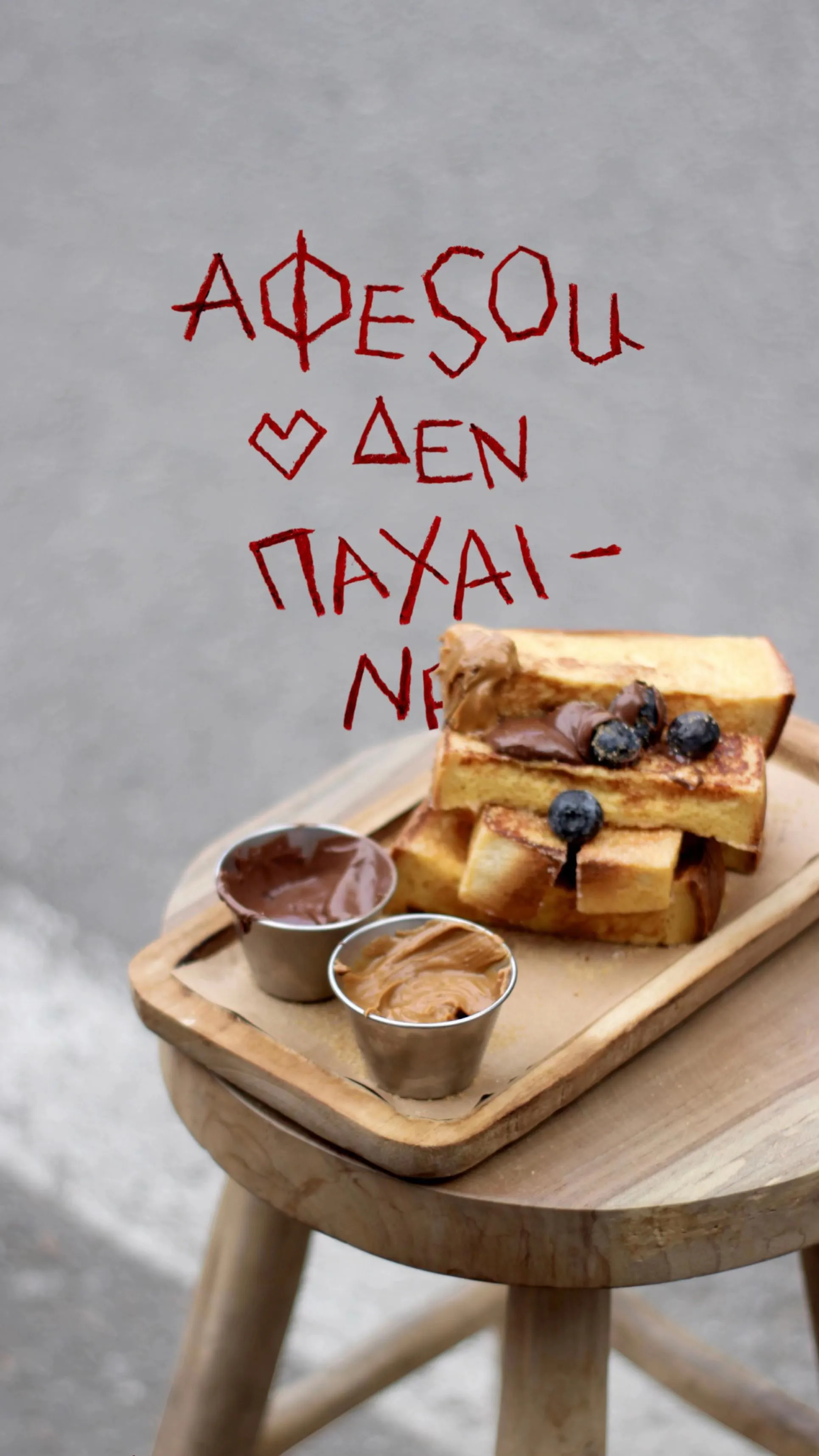 Γαλλικό τοστ με μύρτιλα σε ξύλινο δίσκο, μπροστά από τοίχο με το σύνθημα «ΑΦΕSOU δεν παχαίνει»
